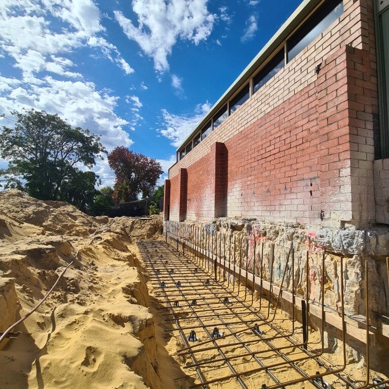 Excavation alongside a brick building, with treated ground beneath the footing